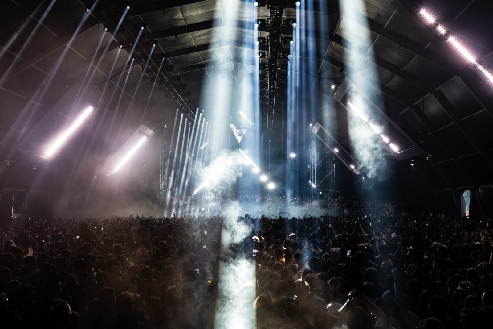 White light beams falling through haze over a dark festival crowd