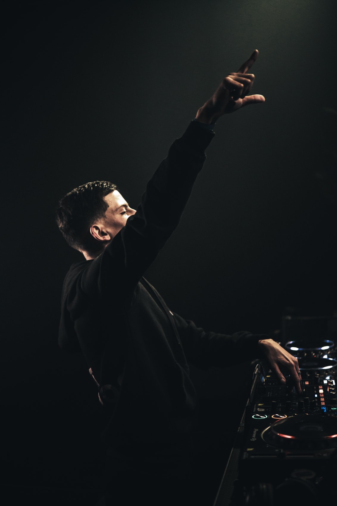 DJ with one arm raised high in a near-black room